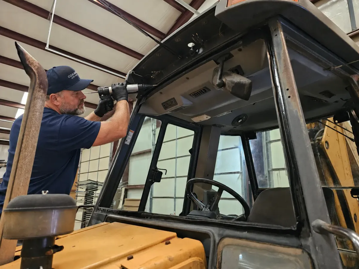 Technician installing glass on heavy machinery in a service workshop