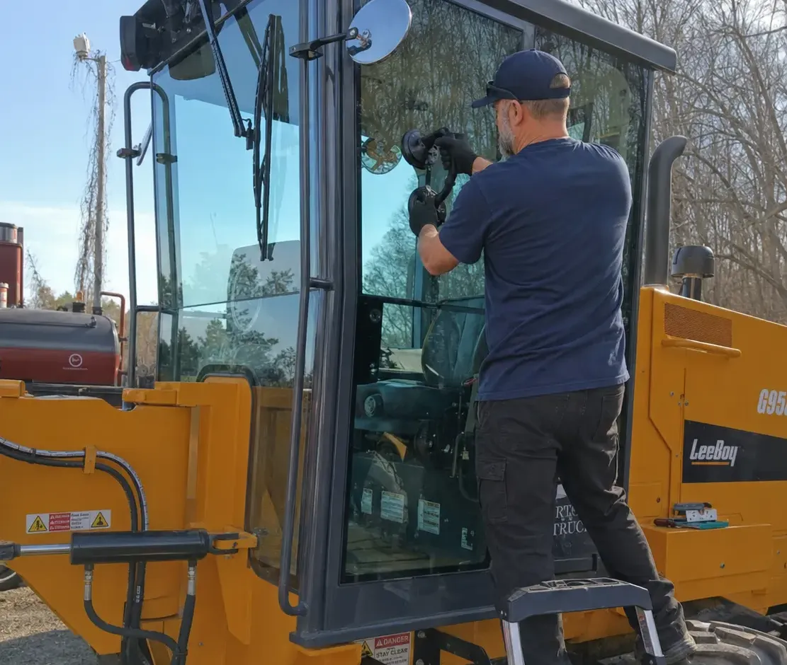 Technician installing replacement glass on a heavy equipment loader cab