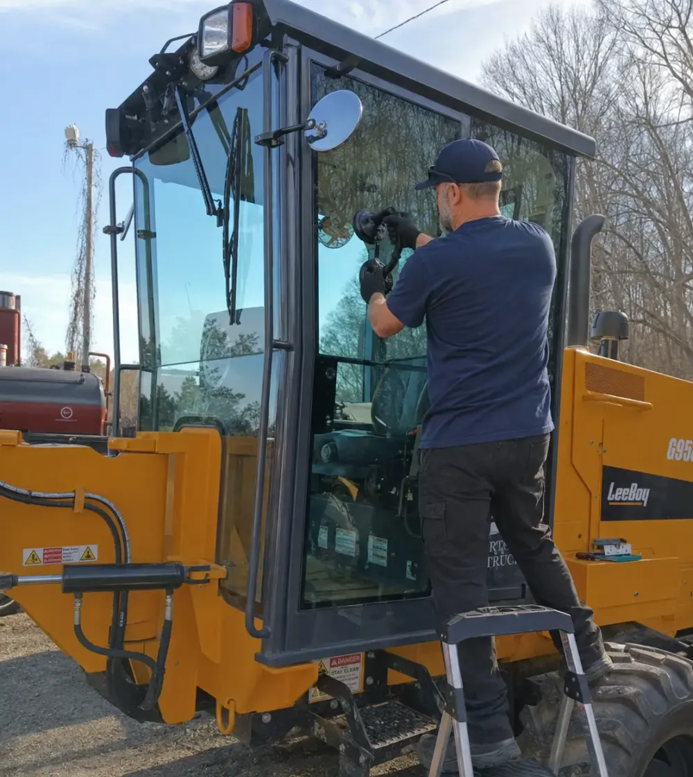 Clear Image technician installing glass on a yellow loader cab on a job site